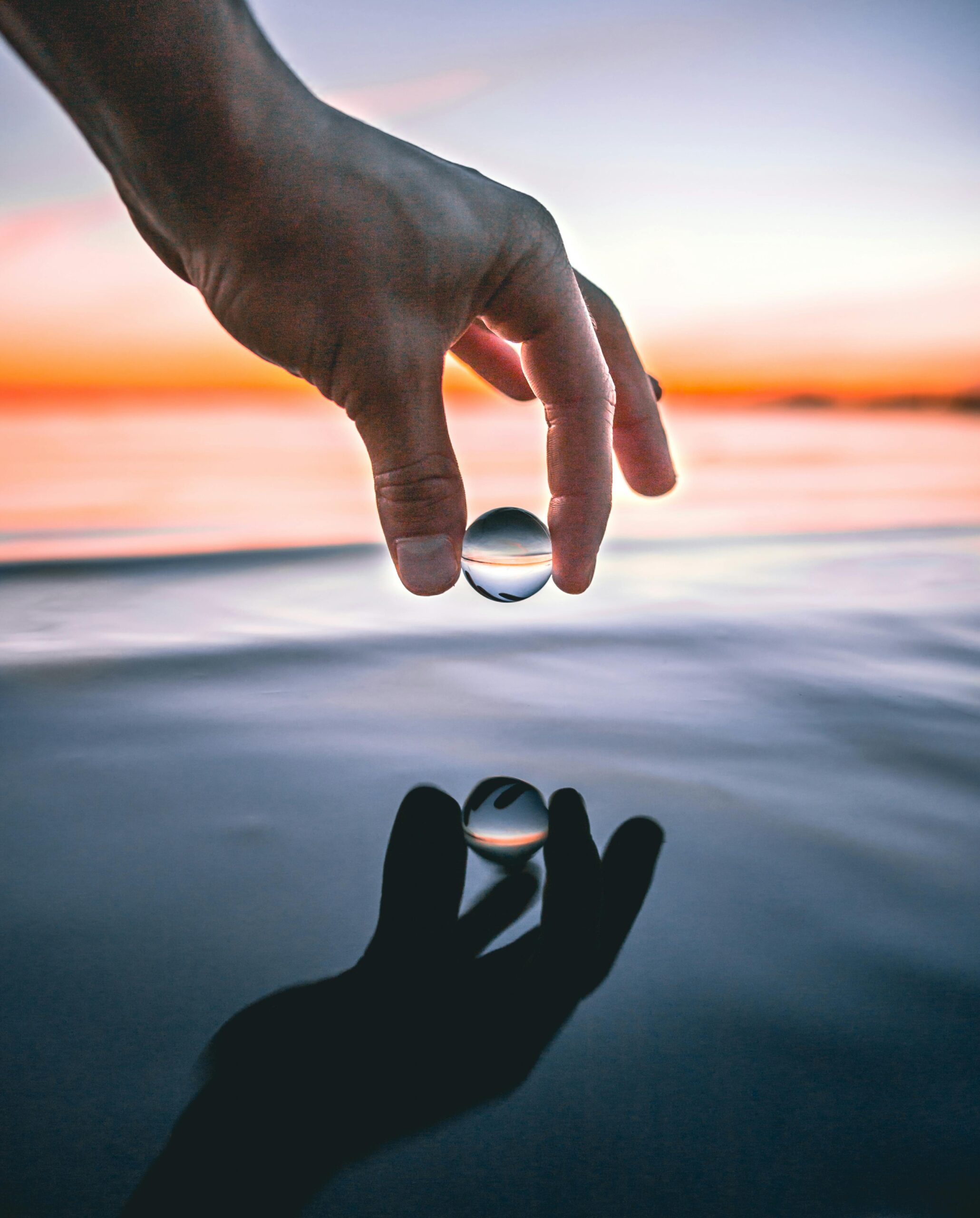 Artistic shot of a hand holding a glass sphere reflecting sunset over the sea in Tallinn, Estonia.